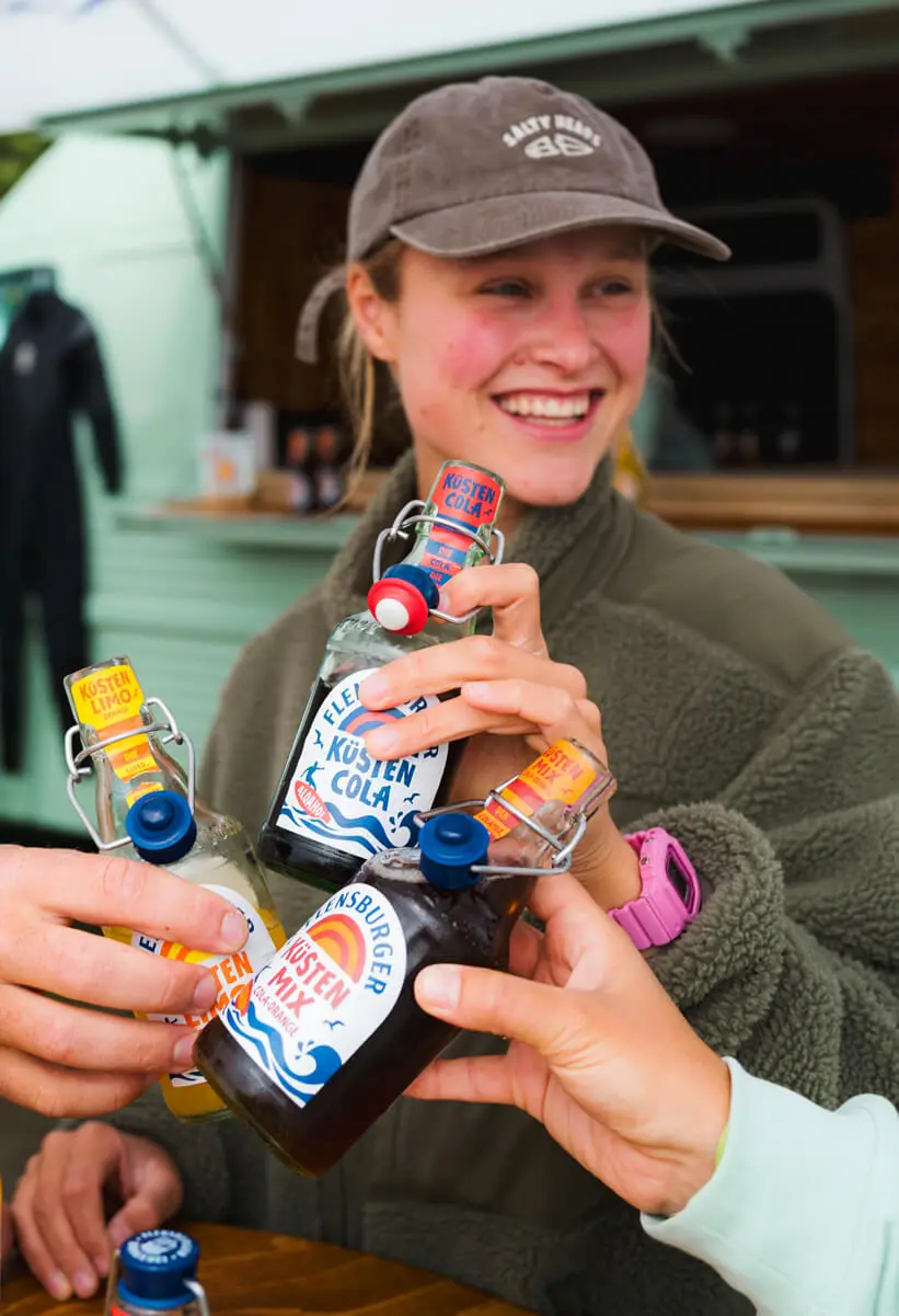 Drei junge Leute stoßen mit Flensburger Küstenlimos an.