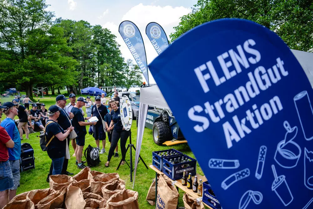 Helfer und Helferinnen genießen das Entertainment nach getaner Arbeit bei der FLENS StrandGut-Mitmachaktion in Flensburg 2024.