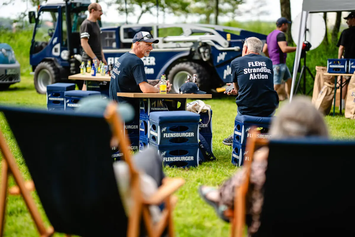 Menschen sitzen auf Liegestühlen nach getaner Arbeit bei der FLENS Strandreinigungsaktion.
