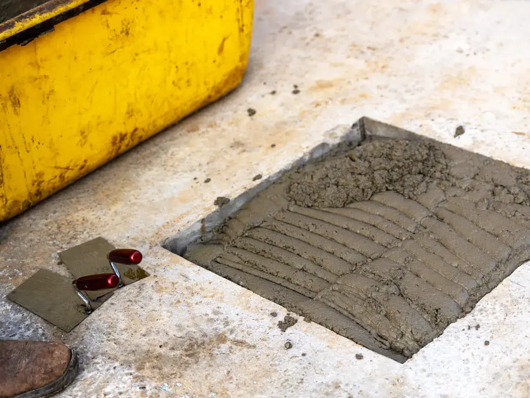 Frisch gegossener Beton auf der Zeitkapsel, daneben ein gelber Bauschuttcontainer und Werkzeug.