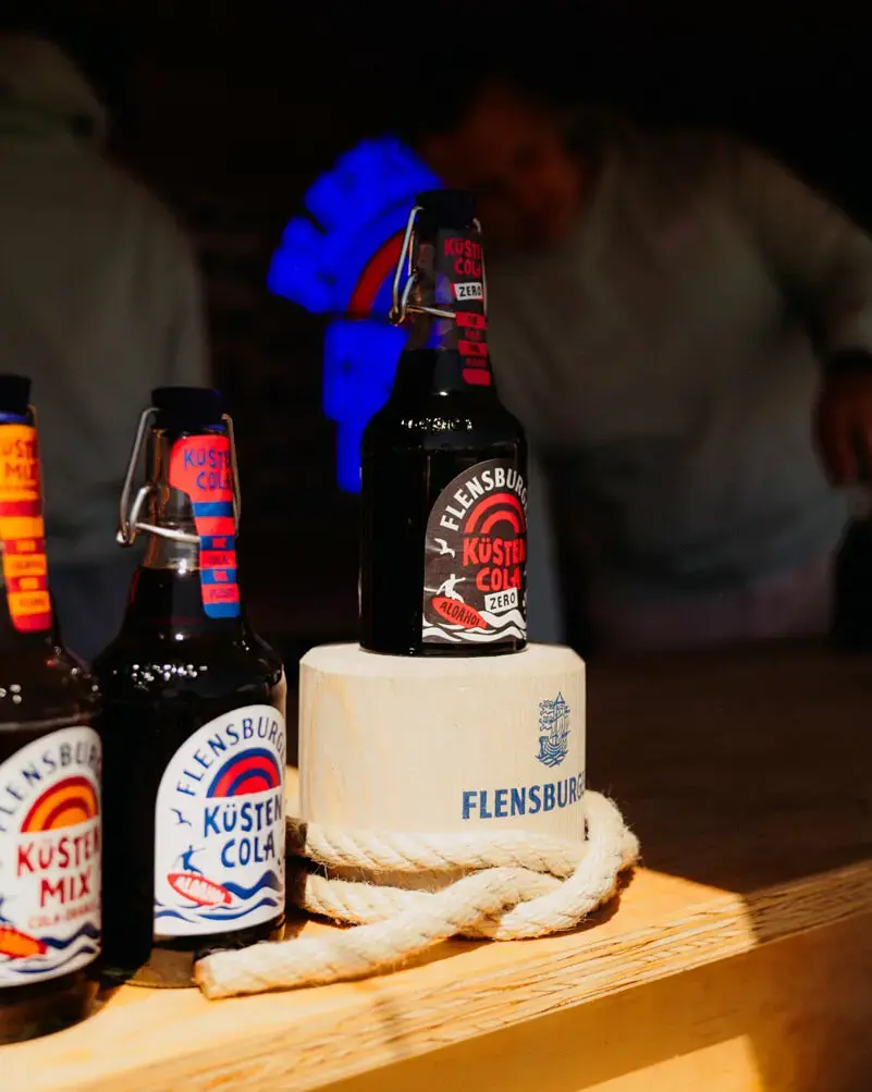 Flensburger-Küstencola-Flaschen auf Holzblock mit Tau auf Theke.