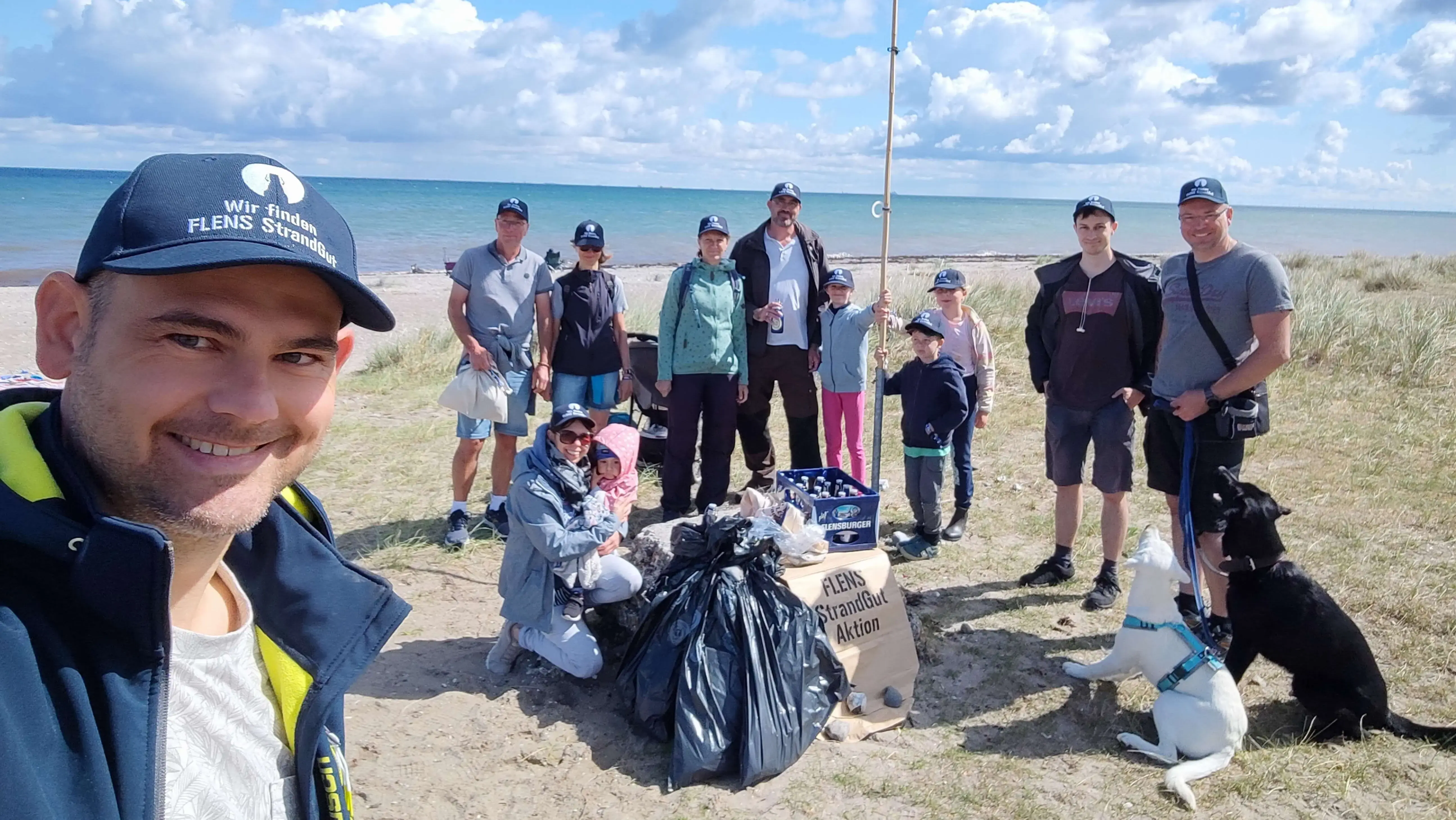 Gruppe von Freiwilligen sammelt Müll am Strand bei sonnigem Wetter im Rahmen der FLENS StrandGut Aktion.
