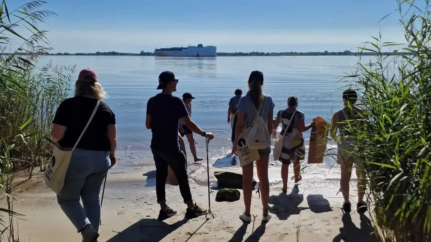 Gruppe von Freiwilligen am Strand bei einer FLENS StrandGut Aktion an einem sonnigen Tag.