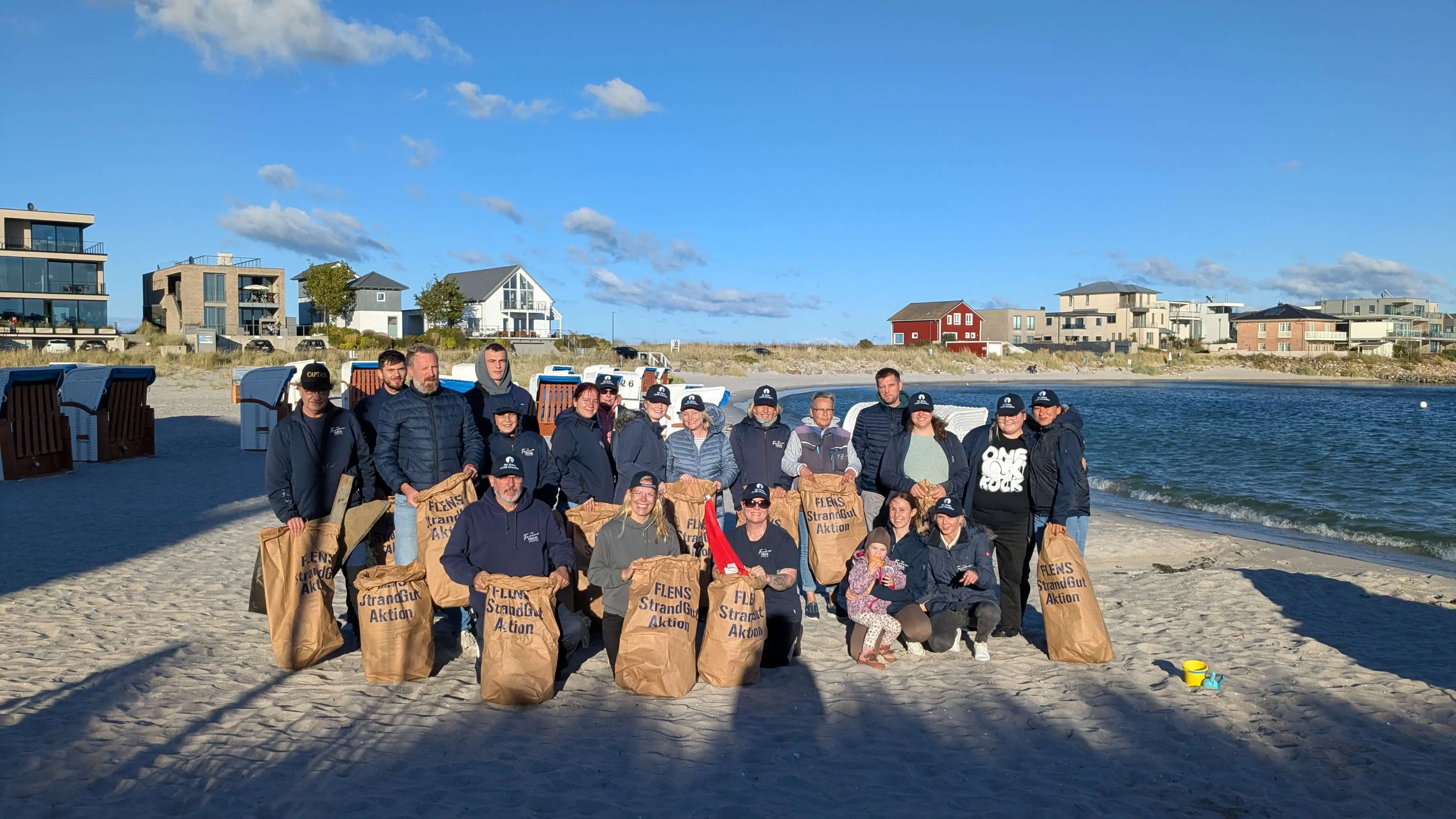 Gruppe von Menschen mit Müllsäcken bei FLENS Strandreinigungsaktion.