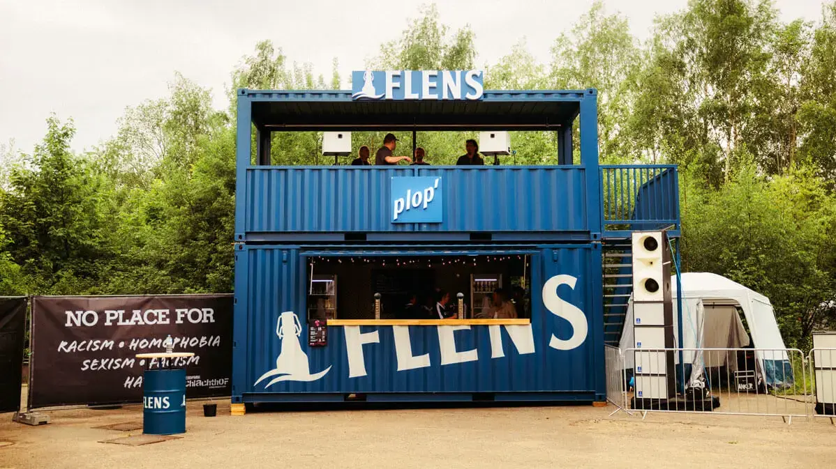 Blauer zweistöckiger FLENS Container mit Pop-up-Bar auf dem Butcher-Jam-Festival 2026 mit Tresen und Lautsprechern.
