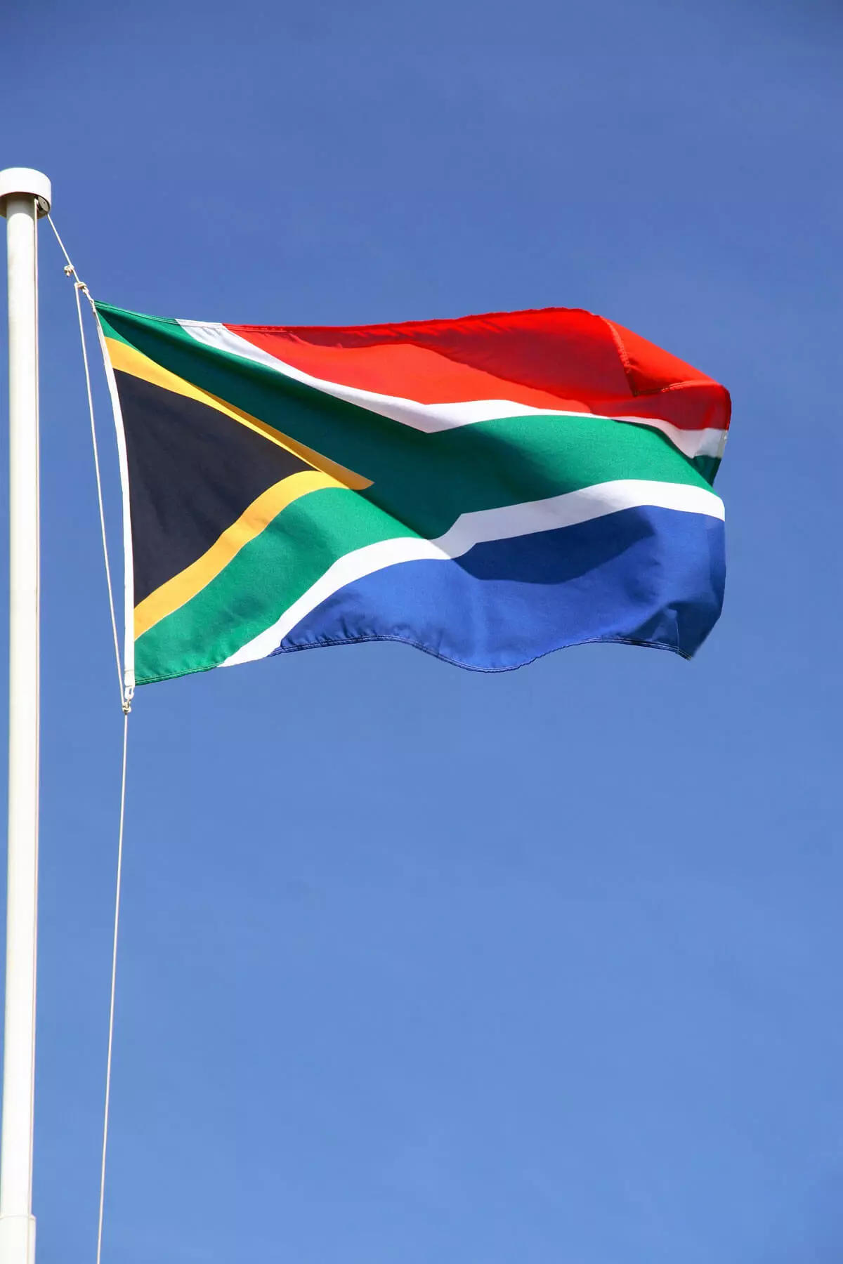 Die gehisste Flagge Südafrikas vor blauem Himmel.