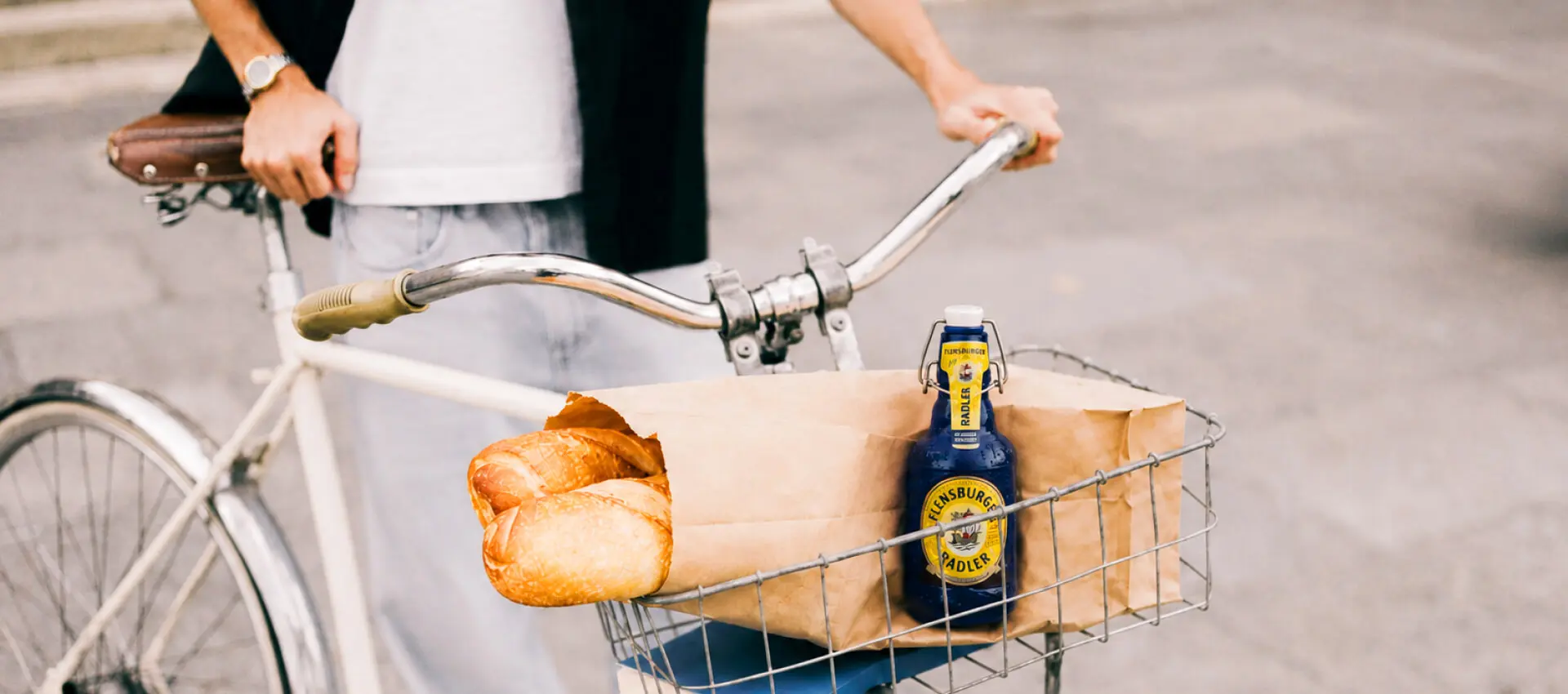Fahrradkorb mit Papiertüte, frischem Baguette und blauer FLENS Radler-Flasche.