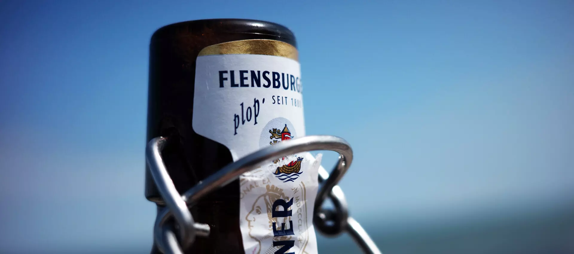 Flaschenhals einer geöffneten Flasche Flensburger Pilsener in Nahaufnahme.