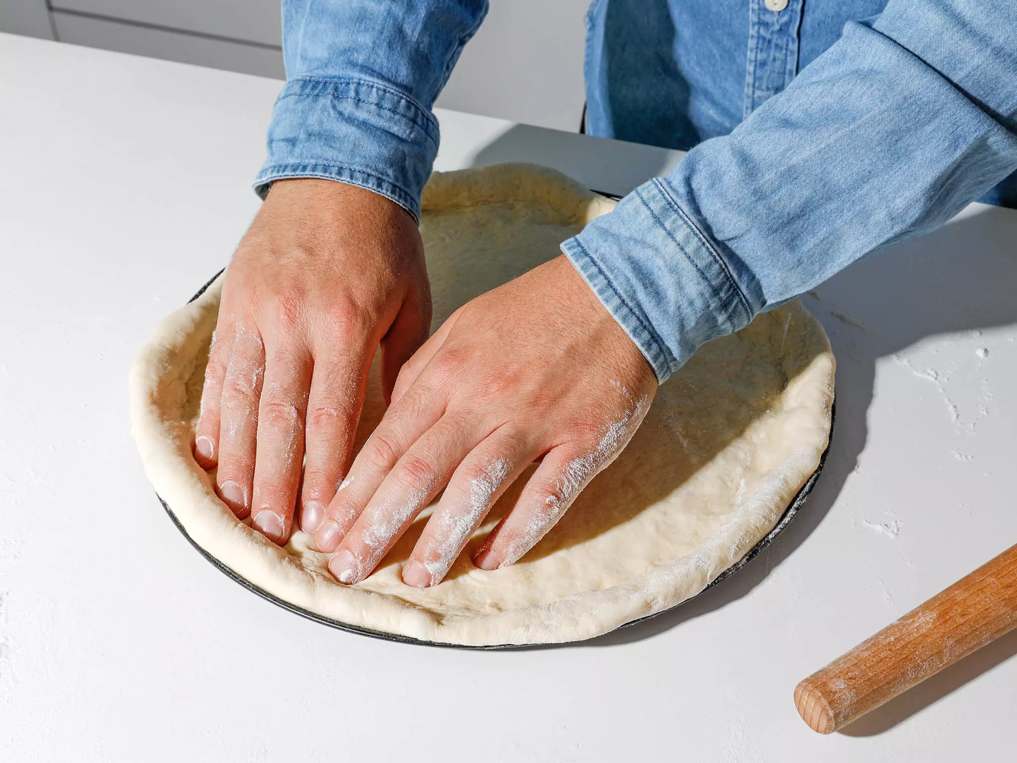 Pizzateig, der in eine Form geknetet wird.