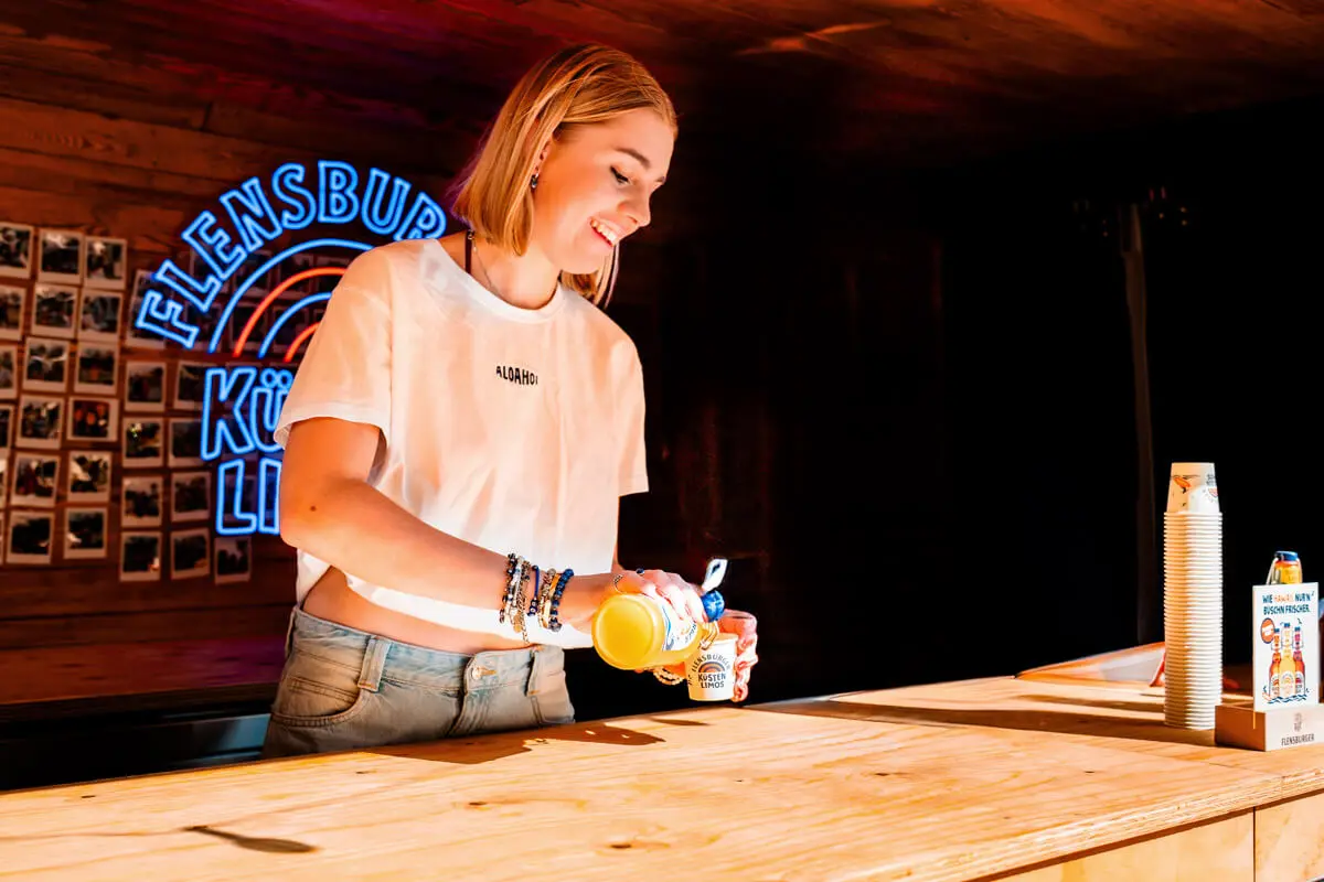 Servicekraft auf dem FLENS Festival 2025 beim Ausschenken von Flensburger Küstenlimos.