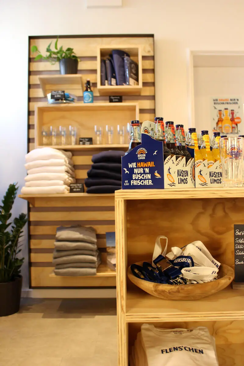 FLENS Merch und Küstenlimos in den Regalen und auf einer Mittelkonsole aus Holz im Plop-Shop.
