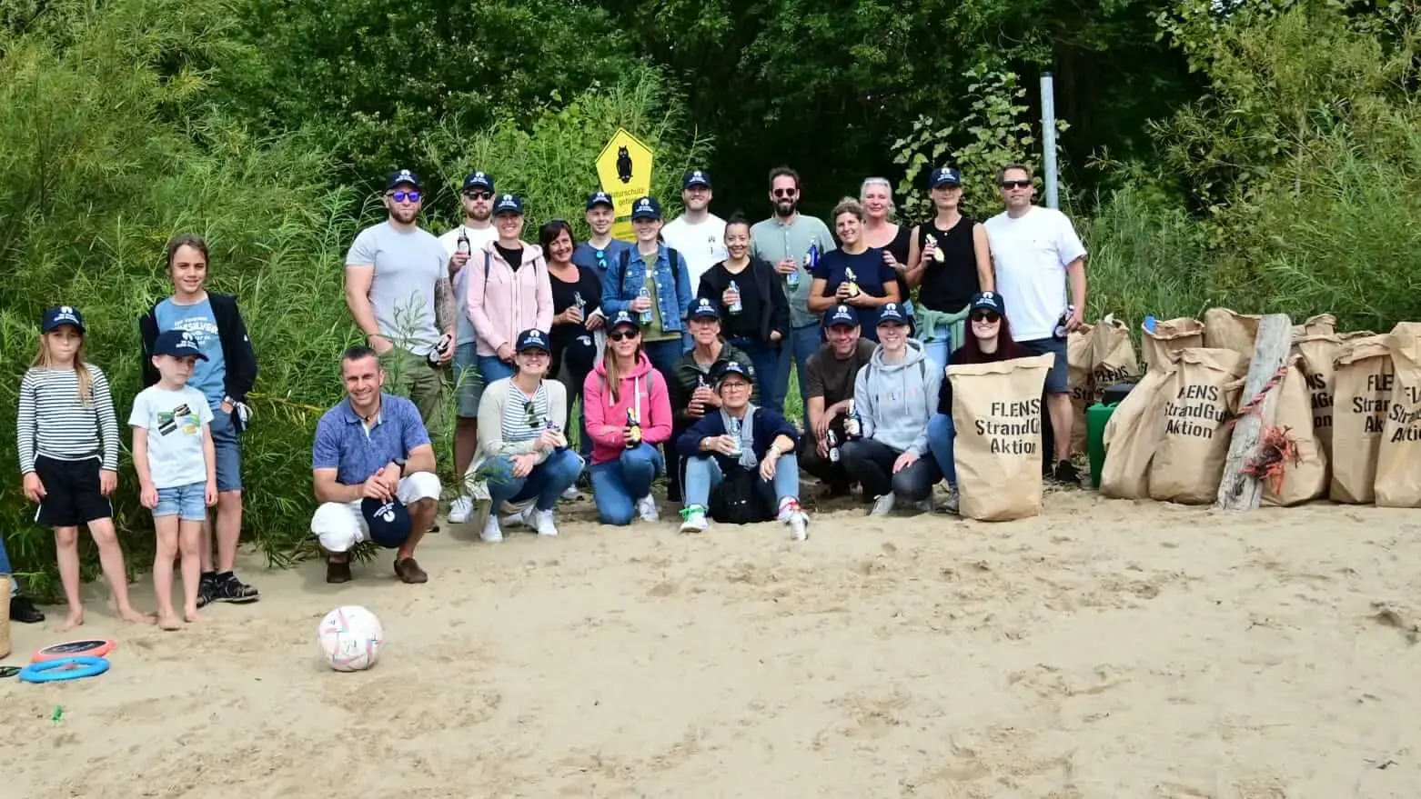 Gruppe von Menschen engagieren sich bei einer FLENS Strandreinigung mit gefüllten Säcken und Greifzangen.
