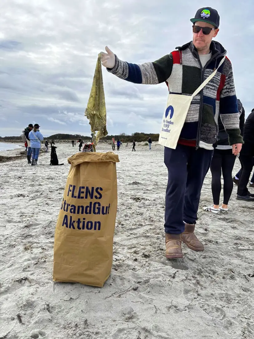 Mann sammelt Müll am Strand während einer FLENS Strandreinigungsaktion.