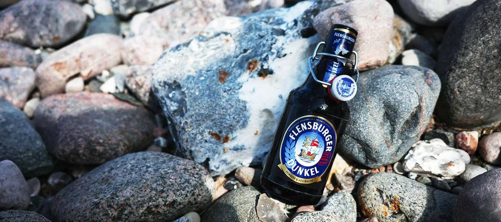 Flensburger-Dunkel-Bierflasche auf kiesigen Strandfelsen.