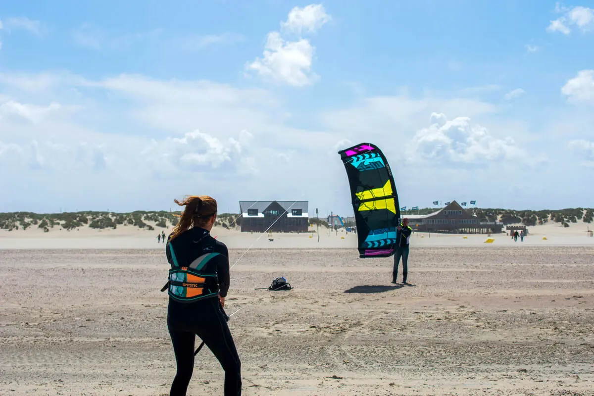 Kitesurf-Kurs am Strand mit Person im Neoprenanzug und buntem Kite bei windigem Himmel.
