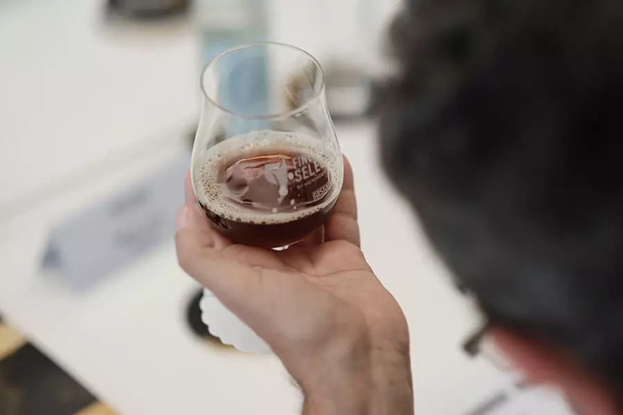 Jury der Finest Beer Selection 2023 bei der Verkostung, Blick über die Schulter auf ein Glas mit einem dunklen Bier.
