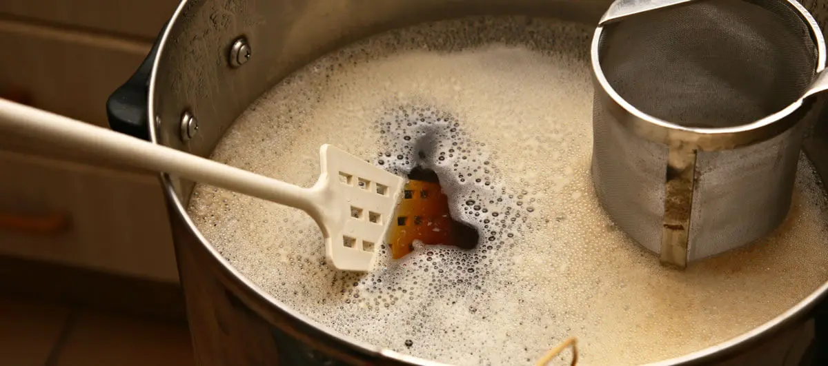 Kochtopf mit schäumender Bierwürze, Schaumlöffel und Hopfensieb.