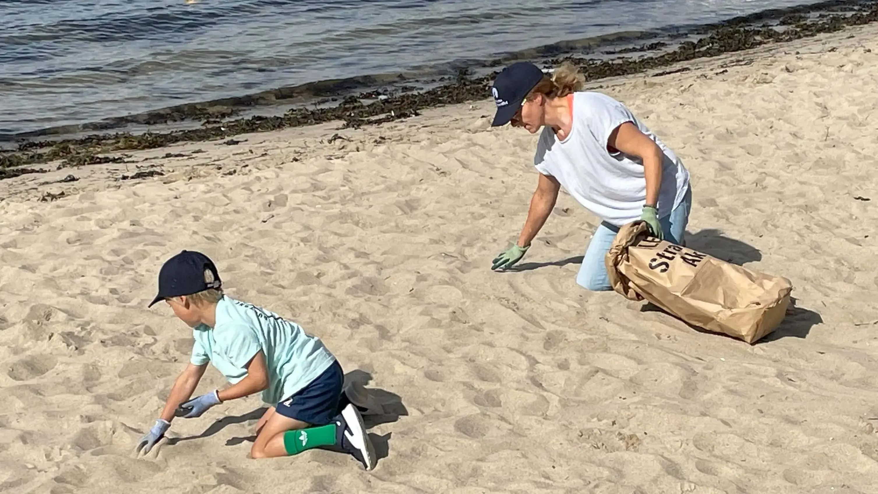 Junge und Frau sammeln Müll am Strand bei einer FLENS StrandGut Aktion.