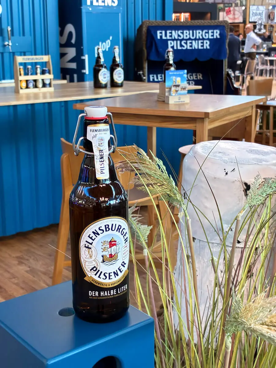 Flensburger-Pilsener-Bierflasche auf blauem Messestand bei einer Biermesse in Rimini.