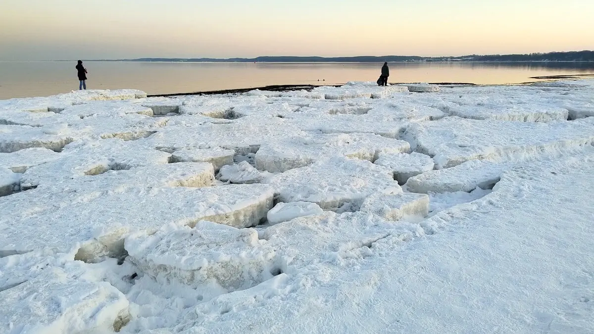 Vereiste Küste mit Eisschollen und Personen, ruhiges Meer bei Winterdämmerung.