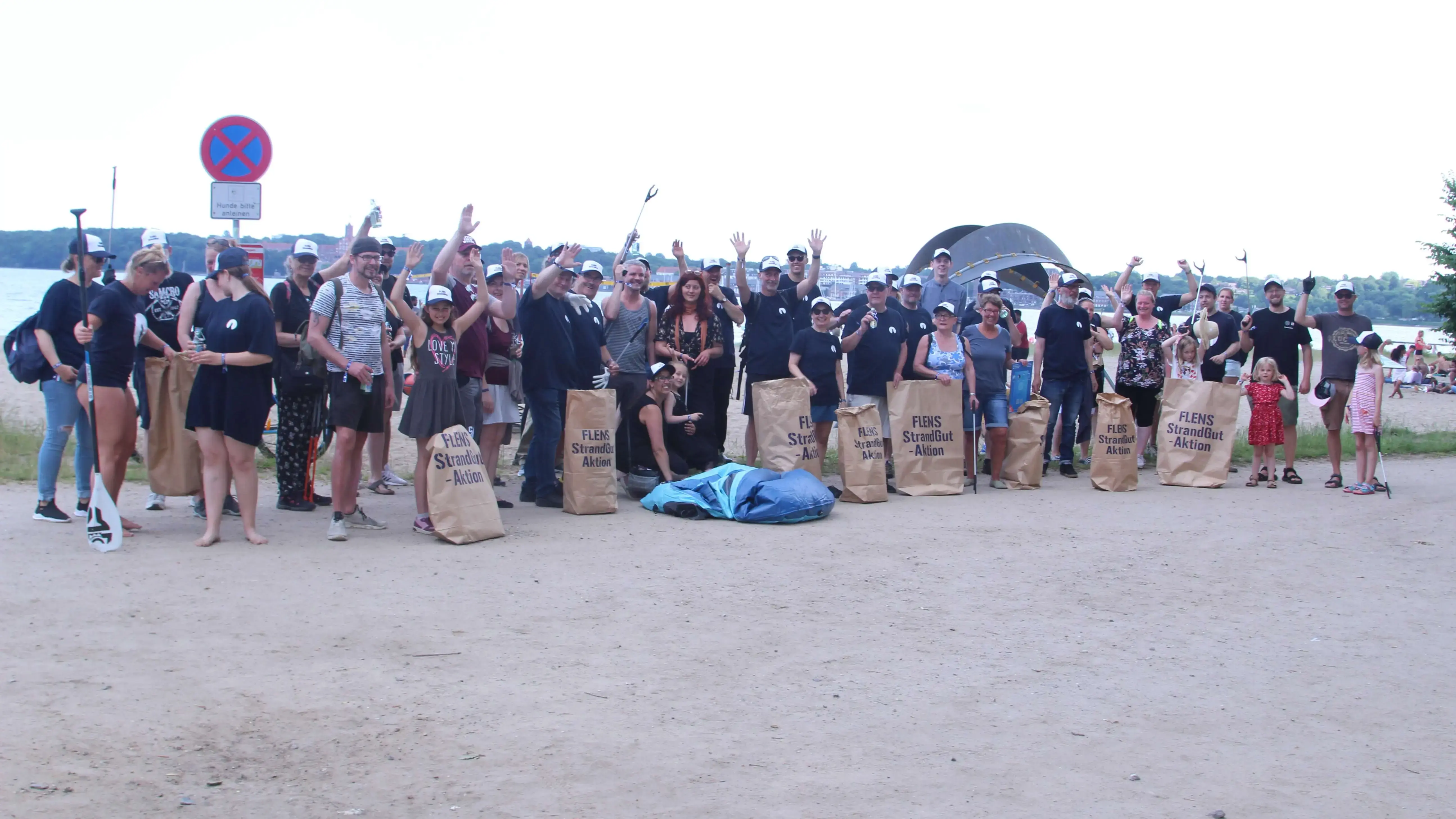Gruppe von Menschen bei einer FLENS Strandreinigungsaktion mit Säcken und Greifzangen.