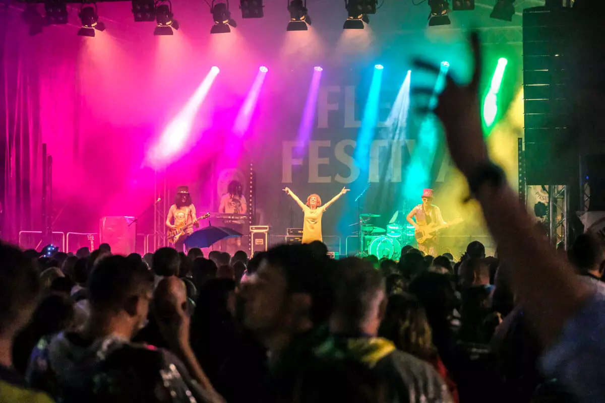 Die Coverband "Hit Radio Show" auf der Bühne beim FLENS Festival 2023 im bunten Licht.