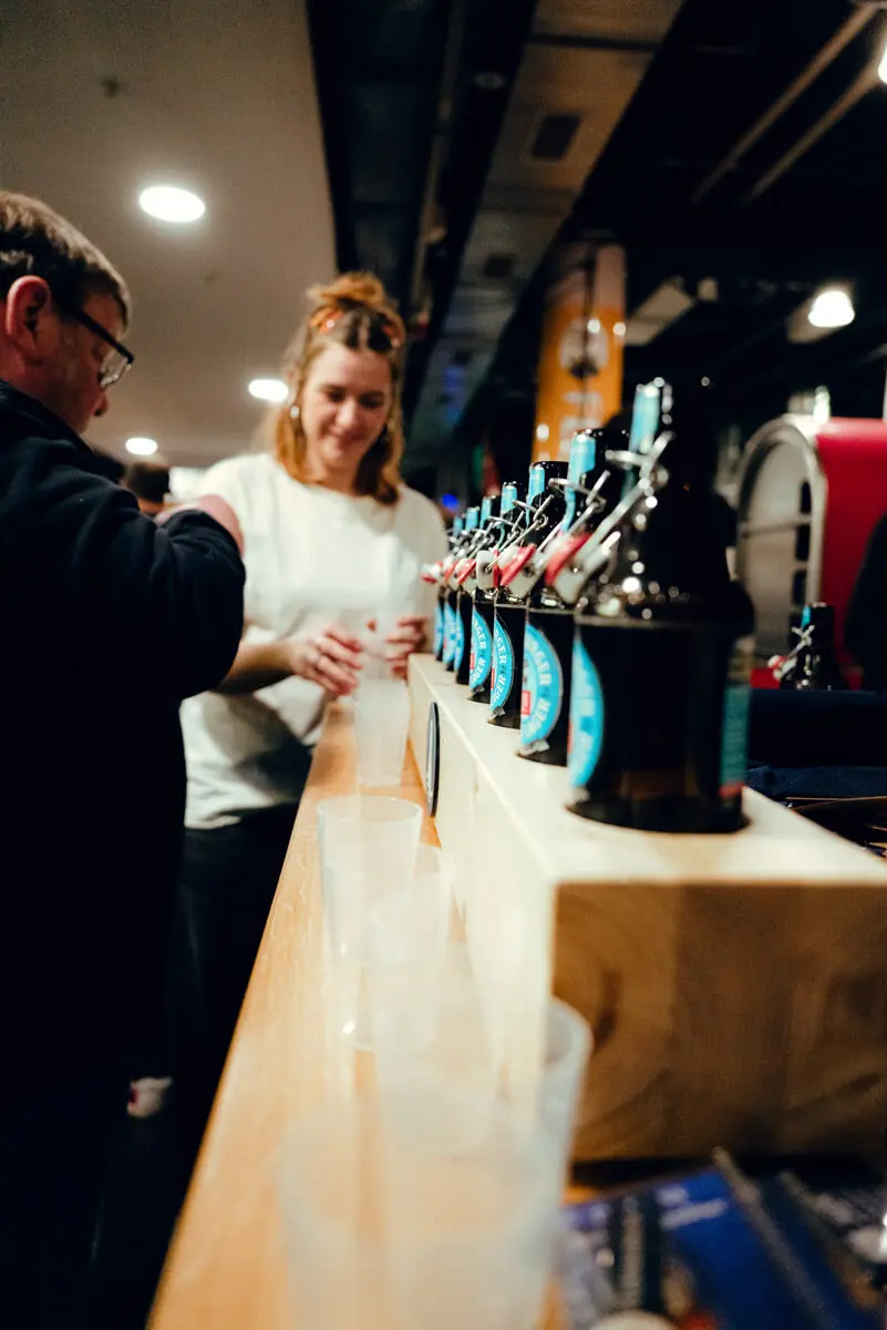 Bierverkostung an Stand: Reihe von FLENS Bier-Bügelverschlussflaschen auf Holzständer.
