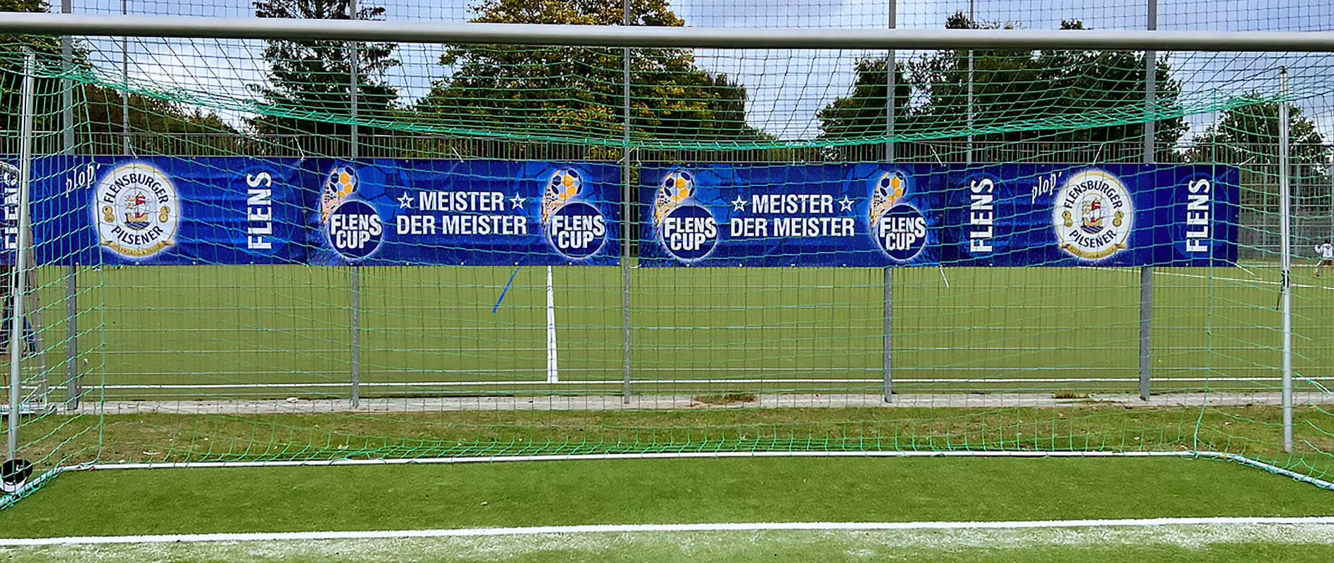 Blaue FLENS Bandenwerbung hinter einem Fußballtor.