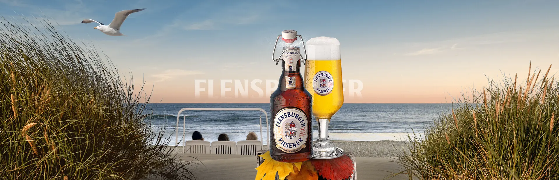 Autumnal beach scenery with wooden pole in the foreground, carrying a bottle and a glass of Flensburger Pilsener beer.