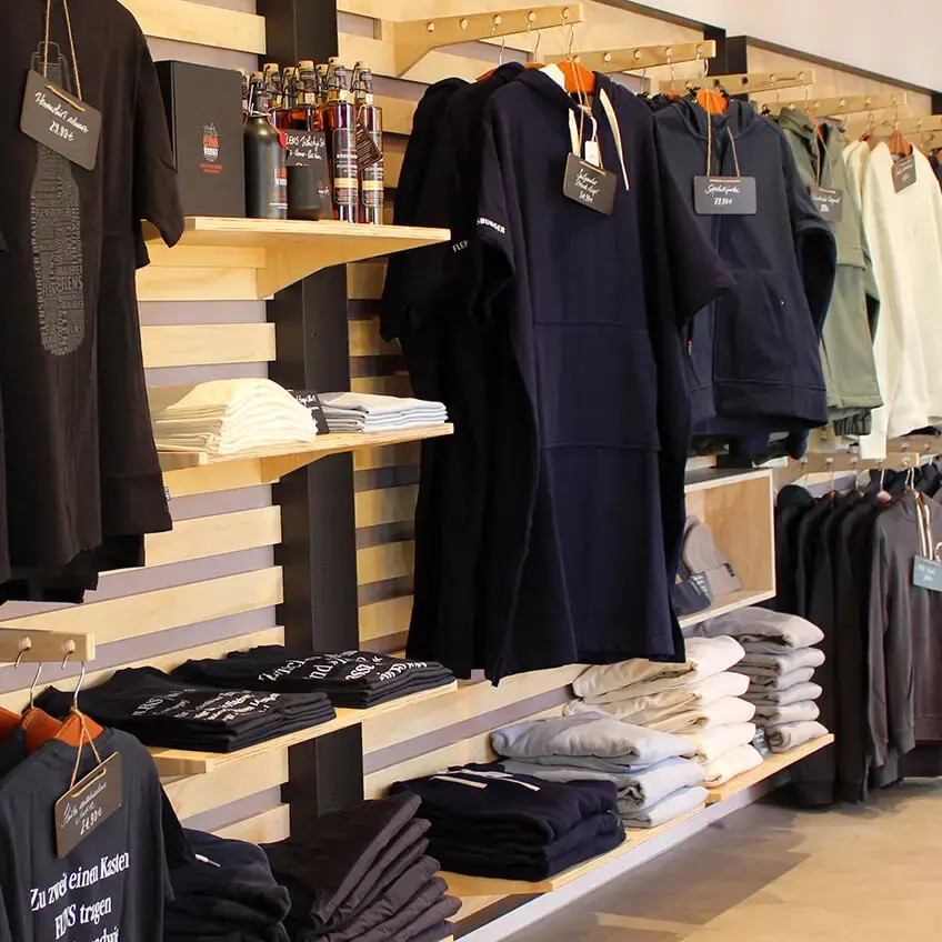 FLENS Klamotten und FLENS Merch an der holzverkleideten Wand im renovierten Plop-Shop.