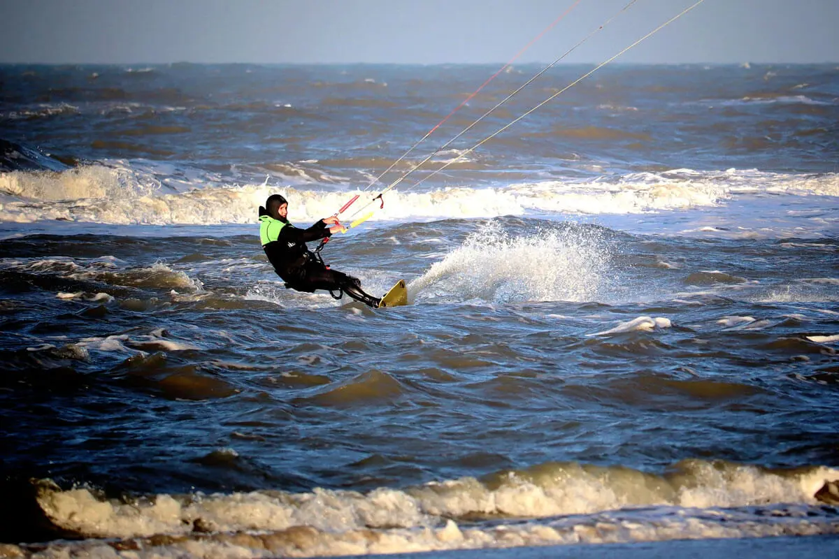 Kitesurfer in Neoprenanzug gleitet über raue See, spritzende Wellen beim Kitesurfen am Meer.