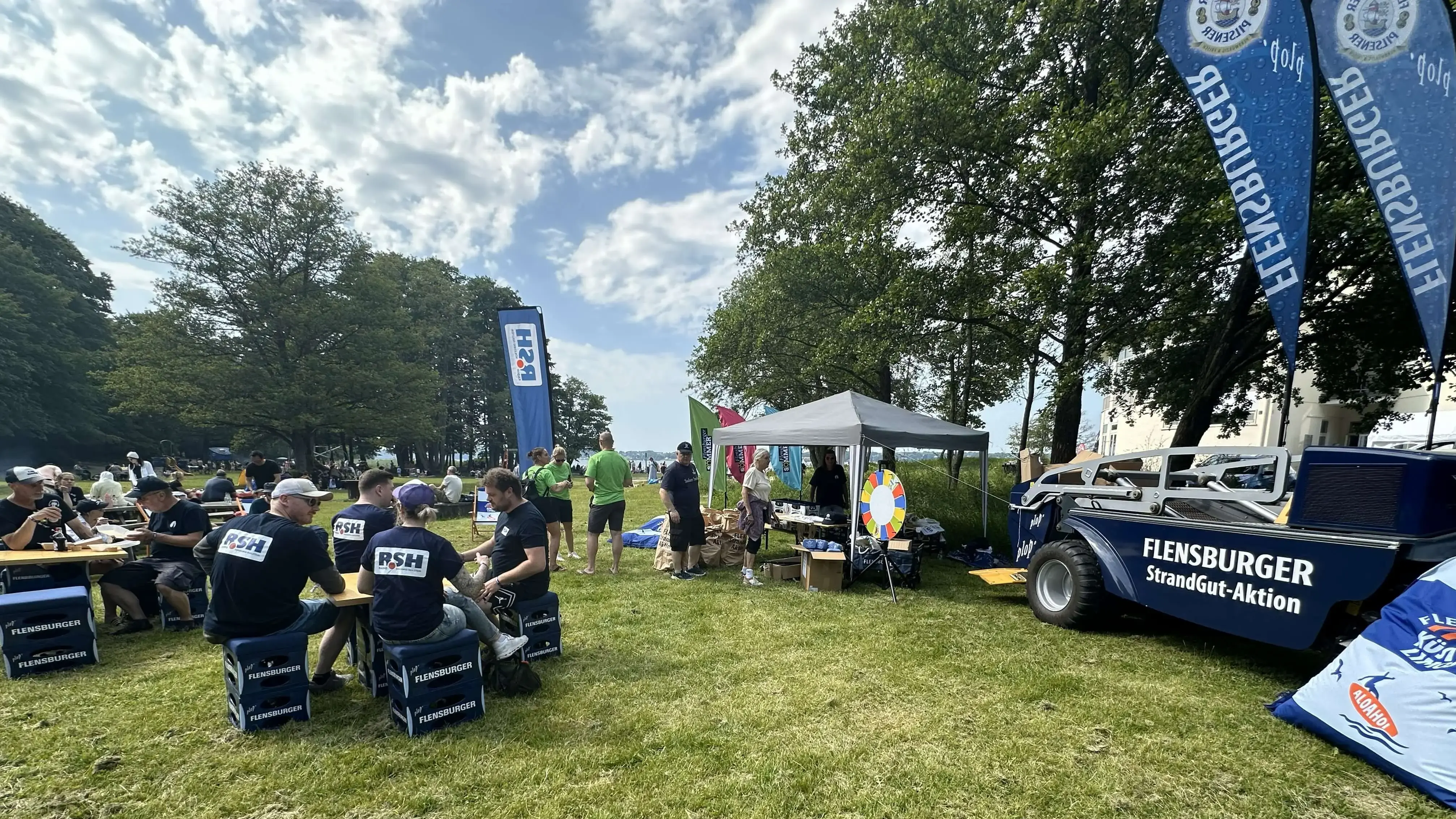 Gruppe von Freiwilligen der FLENS StrandGut Aktion, die nach getaner Arbeit an Tischen sitzen und Flensburger Getränke genießen.