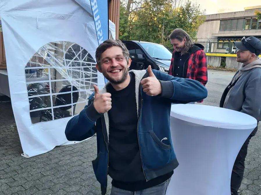 Der glückliche Gewinner gibt Daumen hoch bei der Grillweltmeisterpary von FLENS mit Zelt und Beachflag im Hintergrund.