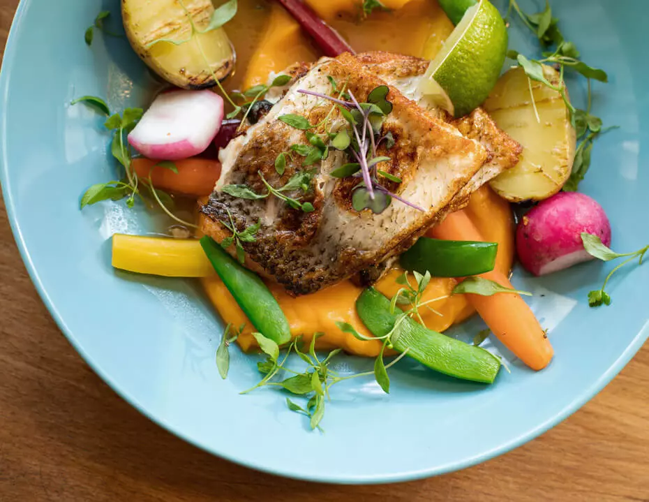 Blauer Teller mit Fischgericht und Gemüse auf Süßkartoffelbrei.