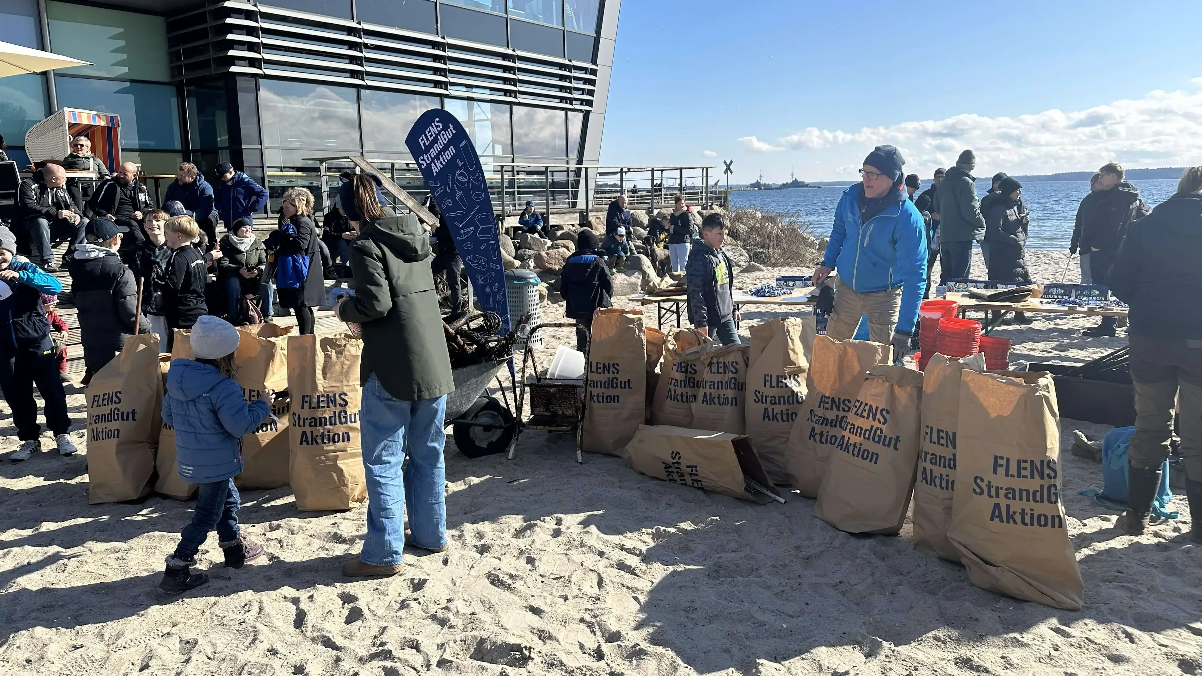 Menschen bei einer FLENS Strandreinigungsaktion an einem sonnigen Tag.