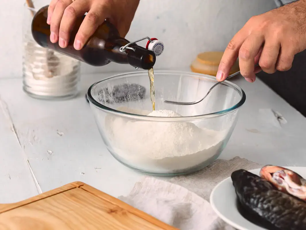 Hände gießen FLENS Bier in Glasschüssel mit Mehl für Bierteig zum Fischpanieren.
