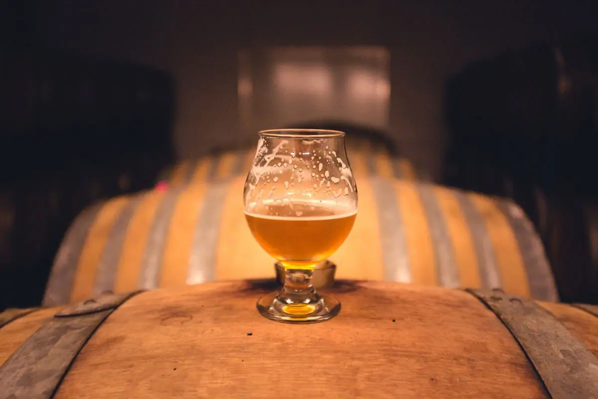 Bierglas auf Holzfässern, stimmungsvolle Beleuchtung im Hintergrund.