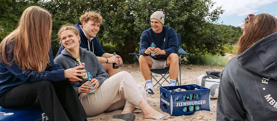 Eine Gruppe junger Menschen am Strand, alle tragen FLENS Merch.