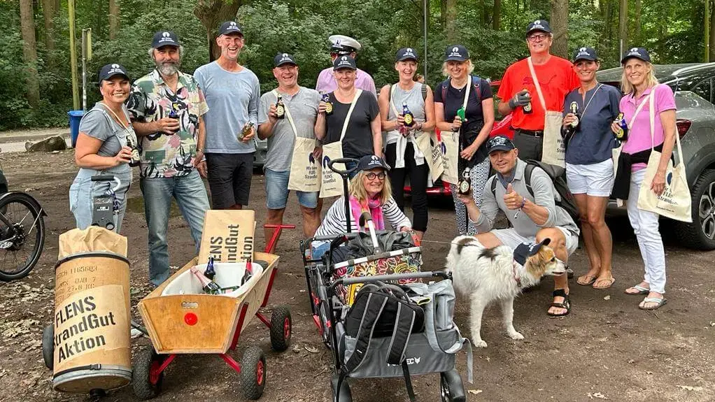 Fröhliche Gruppe von Freiwilligen mit FLENS Flaschen bei einer FLENS StrandGut Aktion im Grünen.