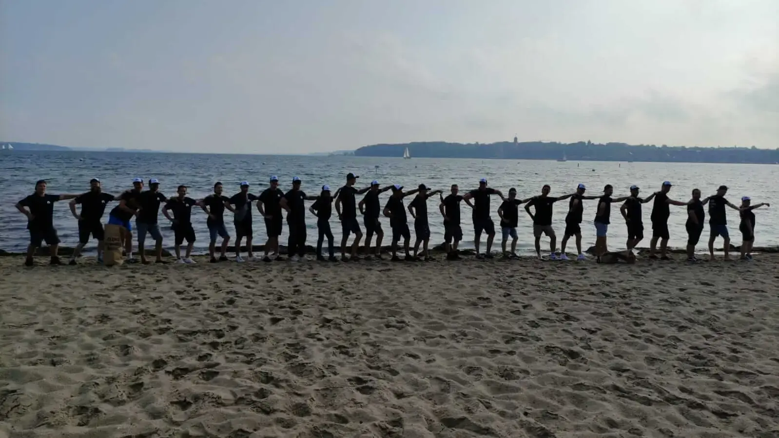 Gruppe von Menschen bildet eine Polonaise am Strand, FLENS Strandreinigungsaktion an der Küste.