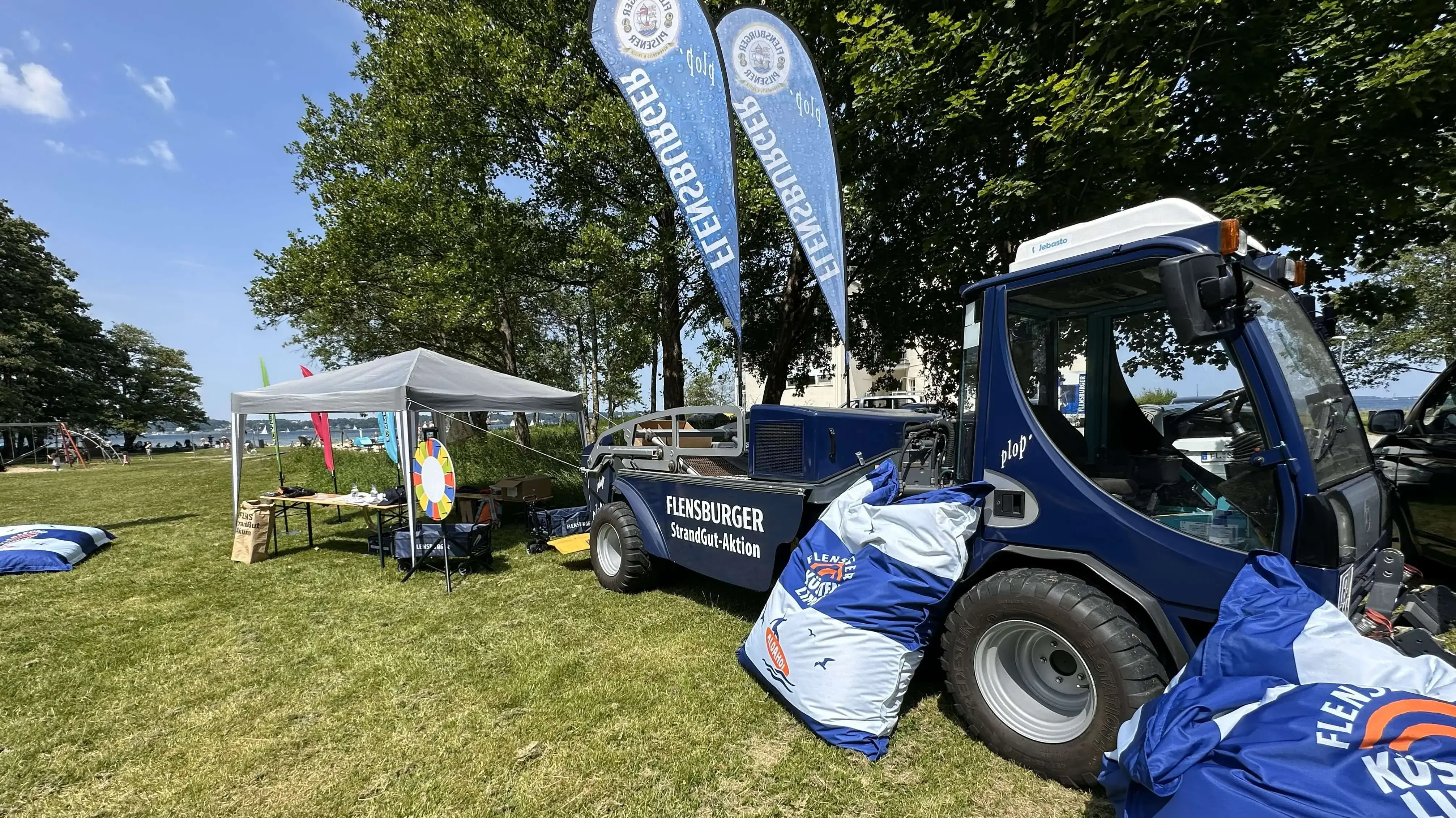 Aufbau der FLENS StrandGut Aktion in Flensburg mit Pavillon, Beach Flags und FLENS Beach Tech (Strandreinigungsfahrzeug) an einem sonnigen Tag.