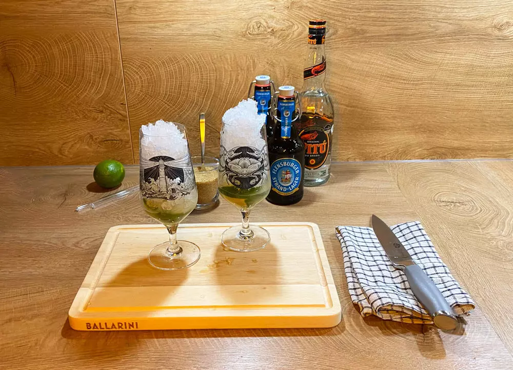 Zwei Biergläser mit Crushed Ice, dahinter Cocktailutensilien.