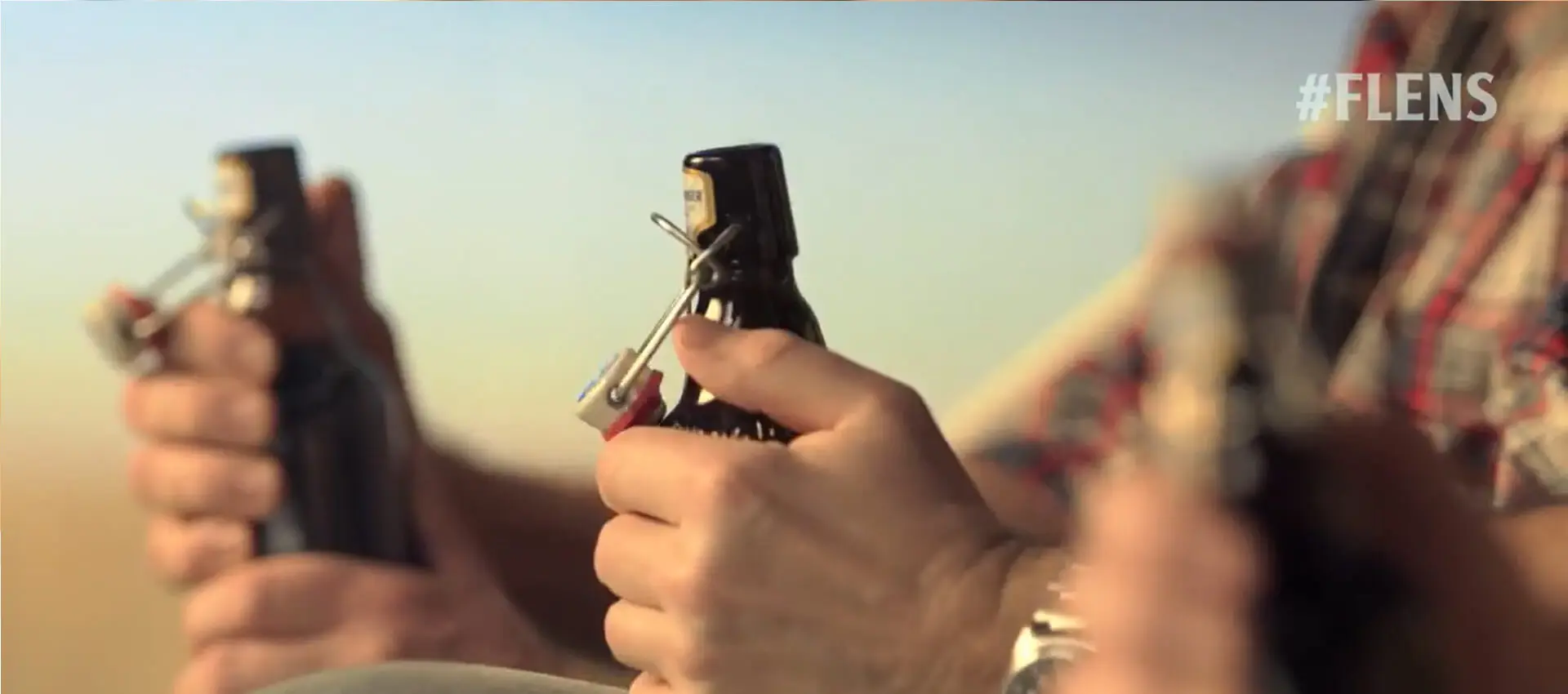 Hände öffnen Bügelverschluss-Bierflaschen im Freien bei Sonnenuntergang