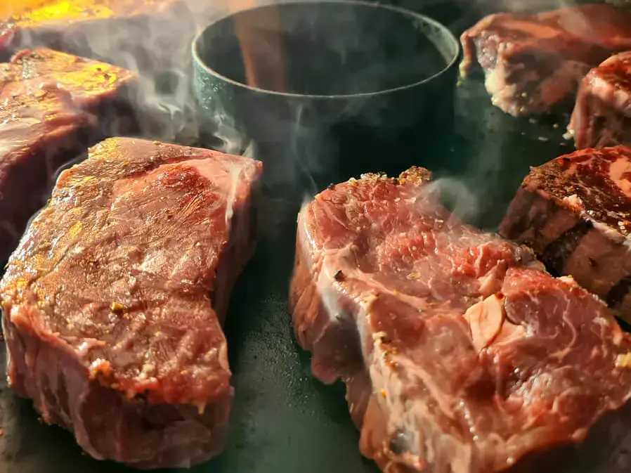 Ribeye-Steaks brutzeln auf heißer Grillplatte mit Dampf und stimmungsvoller Beleuchtung.