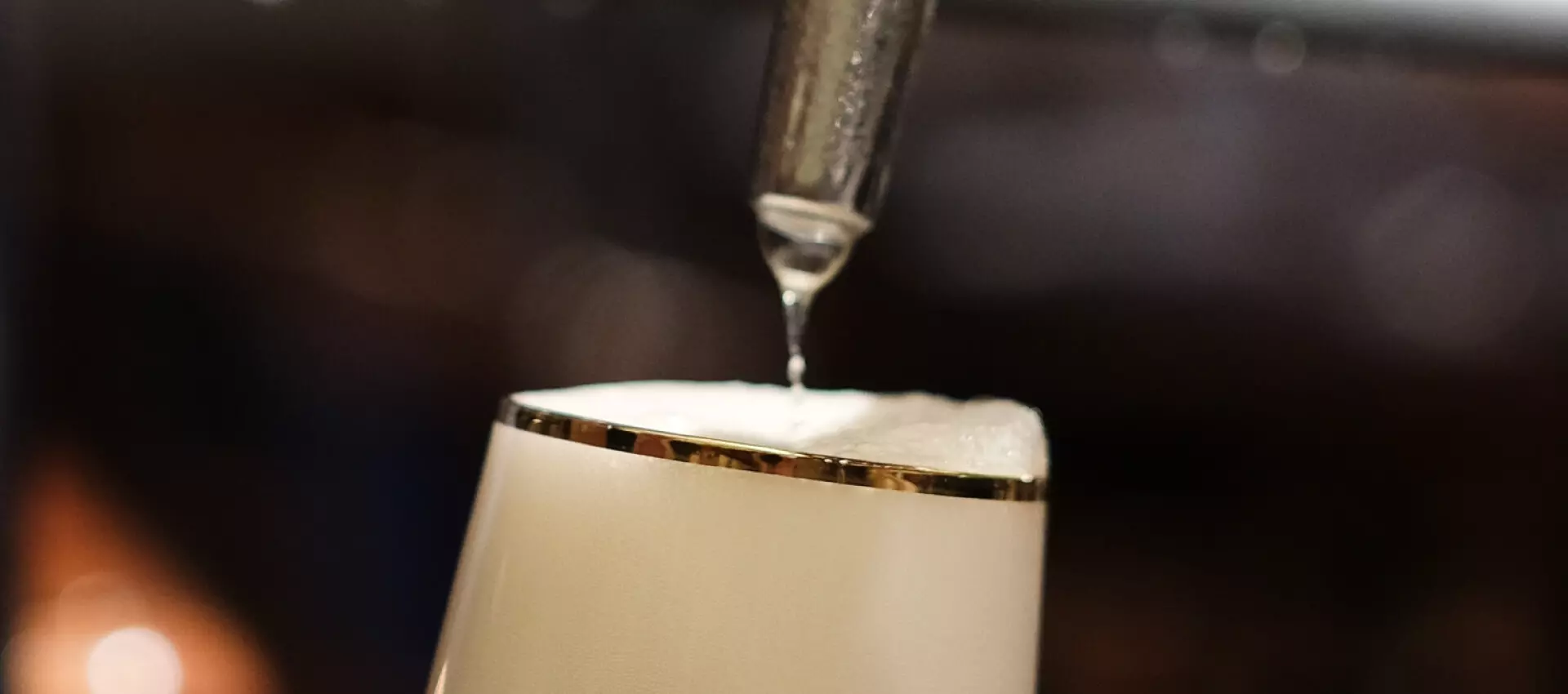 Makroaufnahme vom Zapfhahn und einem Bierglas, ein Tropfen Flüssigkeit fällt auf die üppige Schaumkrone.