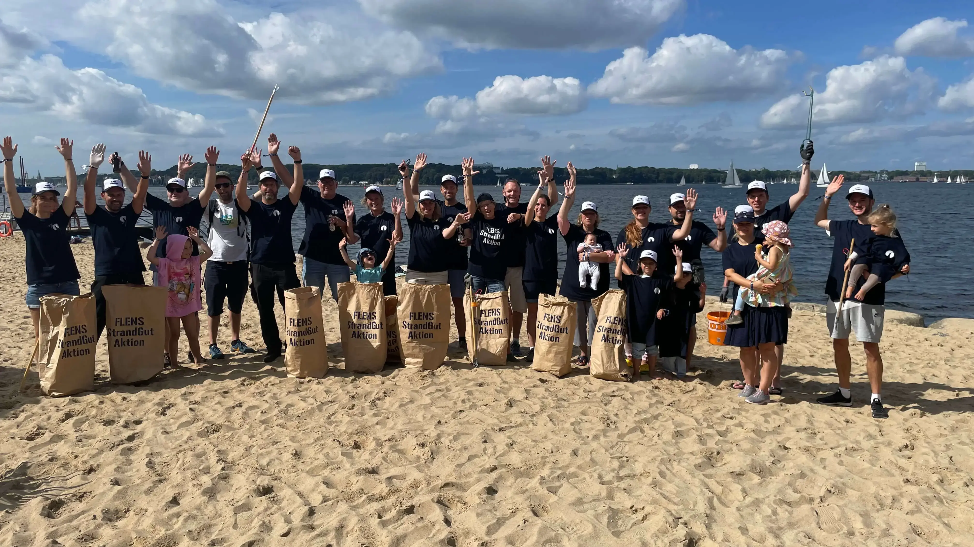 Gruppe von Freiwilligen mit Säcken bei einer FLENS Strandreinigungsaktion am Sandstrand.