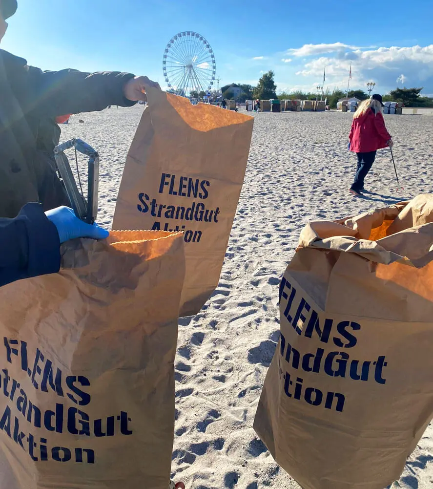 FLENS Müllsammelaktion am Strand mit Personen und Riesenrad im Hintergrund.