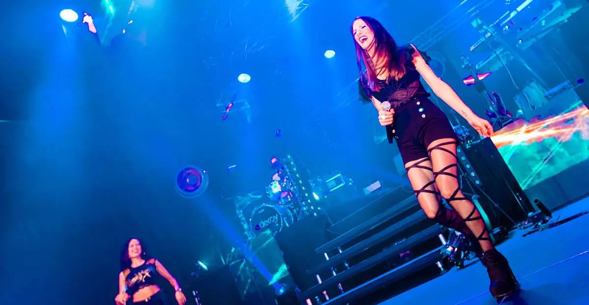 Pressebild der Coverband DECOY: Frau sing auf blau beleuchteter Bühne.