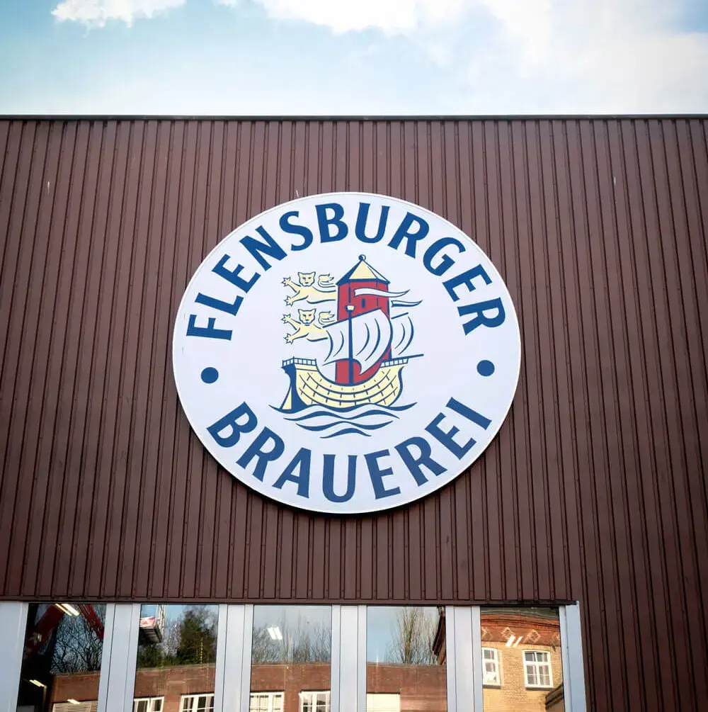 Brauereilogo der Flensburger Brauerei mit Segelschiff an brauner Fassadenwand am Gebäude der Abfüllung.