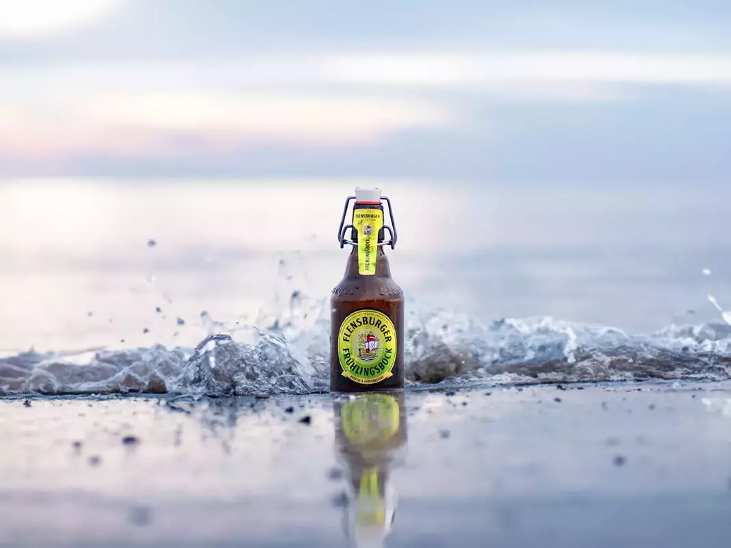Eine Flasche Flensburger Frühlingsbock steht in der Brandung am Meer in der Welle.